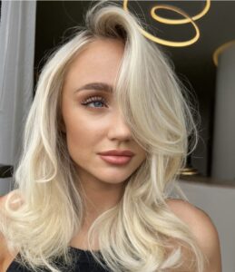 Side-parted shoulder-length wavy blonde hair with big waves, featuring kasey lee blonde specialist low maintenance look.